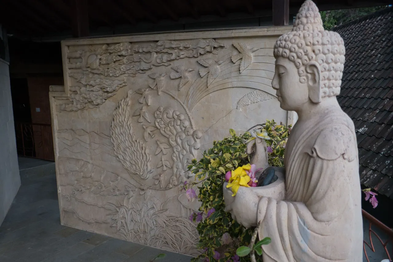 Carved stone wall with Buddha statue and offering flowers