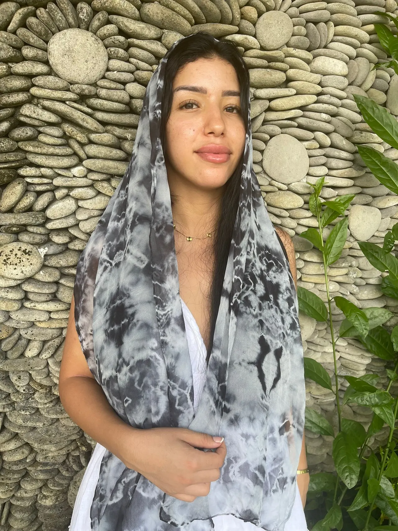 Guest wearing a grey hand-dyed scarf against a river-stone wall