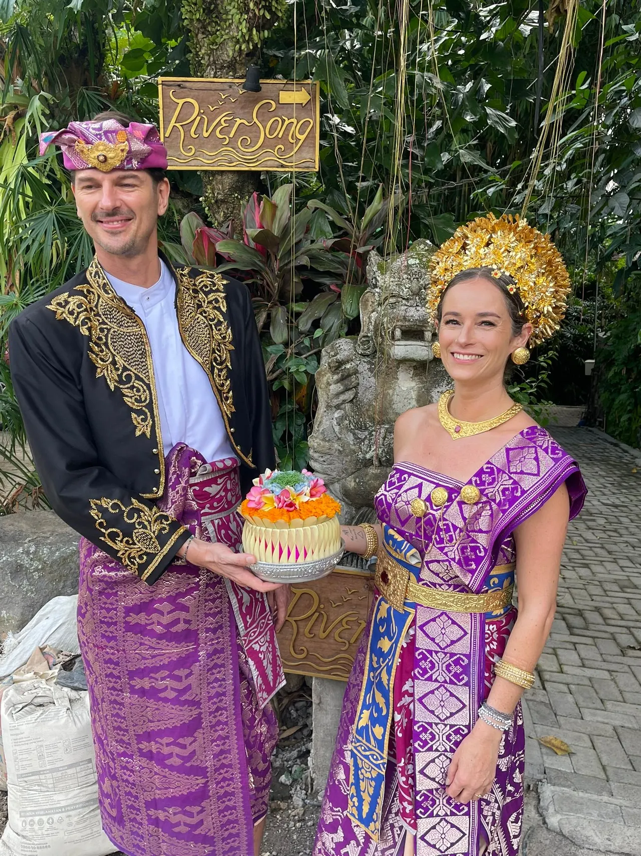 Couple dressed in traditional Balinese ceremonial attire holding an offering