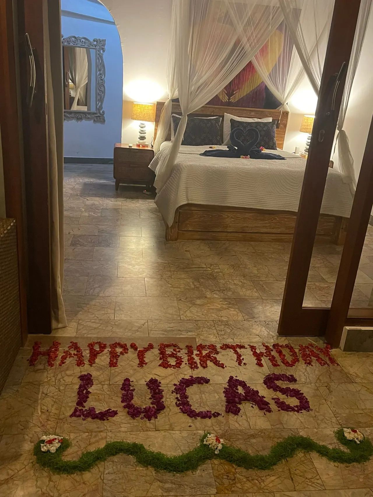 Happy birthday spelled in red petals on a bedroom floor