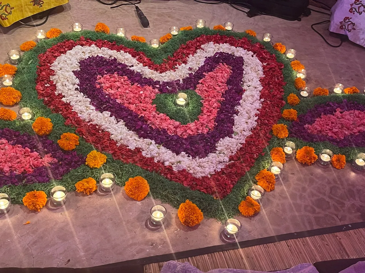 Heart of red, pink and violet petals surrounded by candles and marigolds